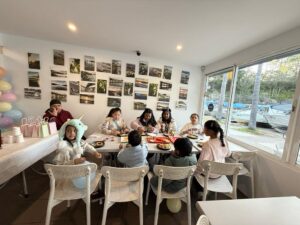Kids and family enjoying meals around a table at Como Marina Bay Cafe with photo wall and waterfront view.